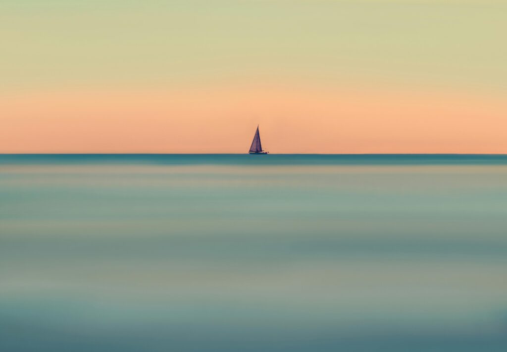 A lone sailboat on a calm ocean with a vivid, tranquil sunset backdrop.