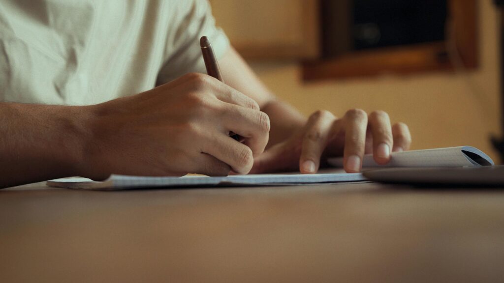 Close-up image of hands writing in a notebook, under warm dramatic lighting, conveying focus.