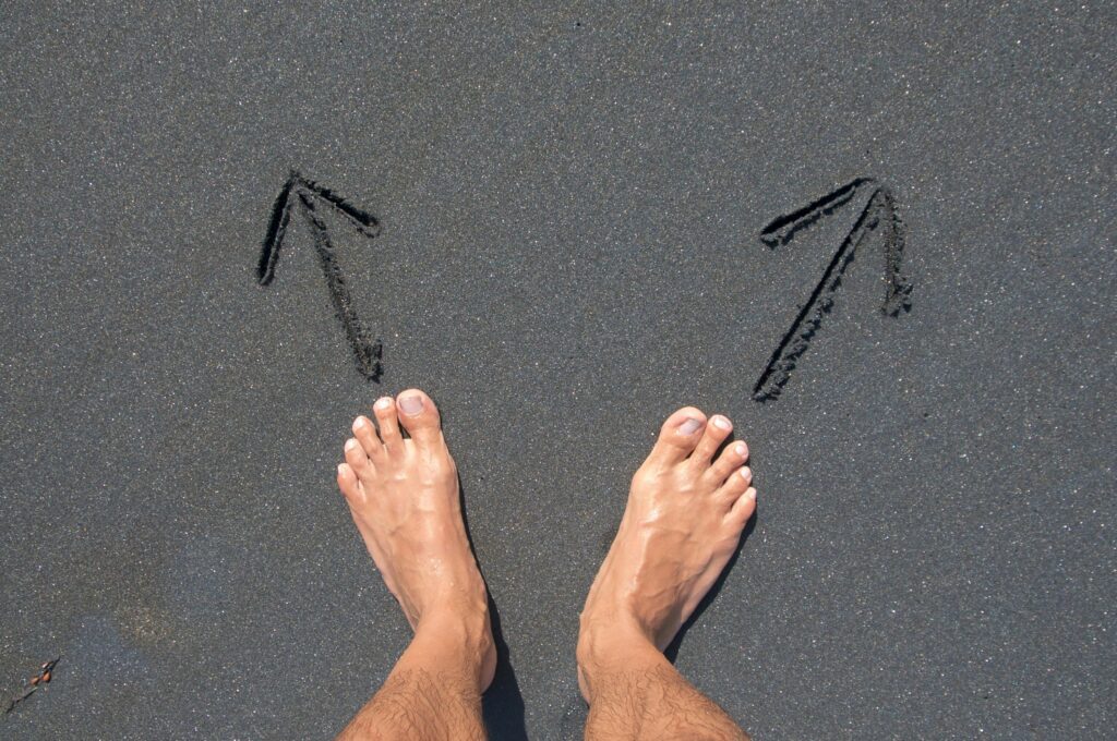 A pair of bare feet on Bali's beach sand with arrows drawn, symbolizing choice and direction.