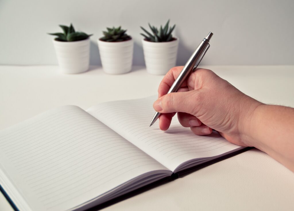 Handwriting in a lined notebook placed on a table with succulent plants in the background representing the structured work of CBT for health anxiety
